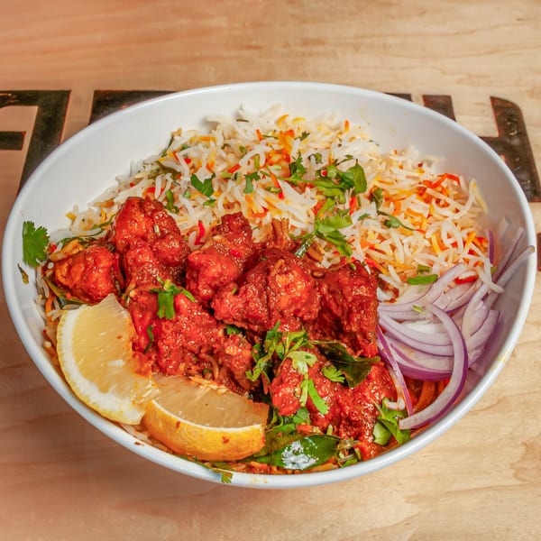 Bharath Cafe's Indian chicken dish with rice, lemon, and red onions in a white bowl.