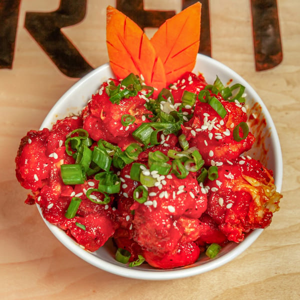 A white bowl filled with bright red Indian-style cauliflower, garnished with green onions and sesame seeds.