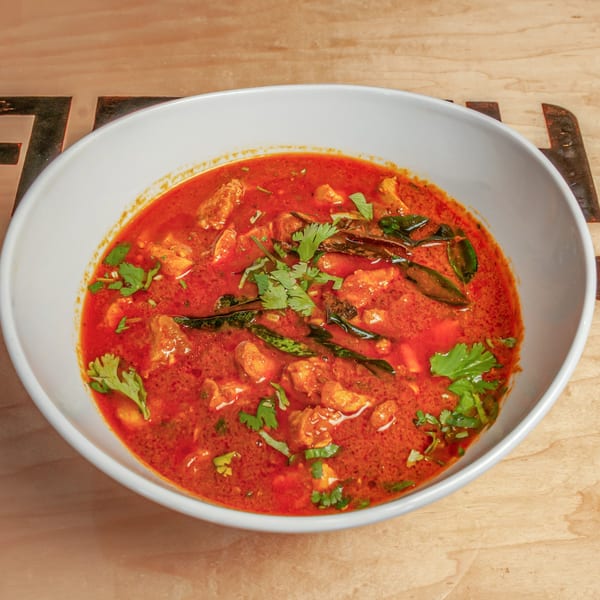 A vibrant red Indian curry with chicken, green chilies, and cilantro in a white bowl.