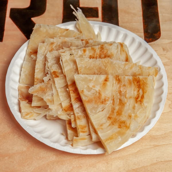 A white paper plate filled with golden-brown, flaky Indian parotta bread cut into triangles.